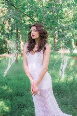 Young attractive girl in a long white dress with a beautiful hairstyle, with white dream catchers...