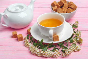 Cup of tea with sugar cubes and flower branches on wooden table close up