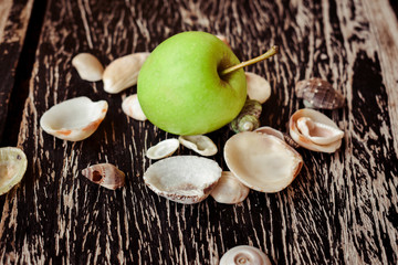 Close up shot of green apple with wooden table background and shells around it.