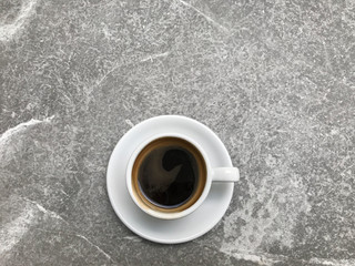 hot black coffee in white ceramic cup and saucer put in the middle of grey and white pattern of rough granite stone table