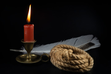 Fototapeta na wymiar Coiled rope with burning candle and quill pen