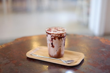 A cup of iced chocolate with salted caramel sauce topped layer is fresh milk on the table with selective focus.