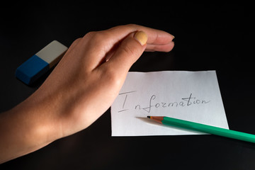 White paper sheet with word "Information" and pencil are on the black background. Female hand is protecting information, near is eraser. Computer Security Day.