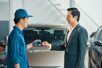 Smiling car service worker in uniform giving electronic key to happy client after repairing his automobile