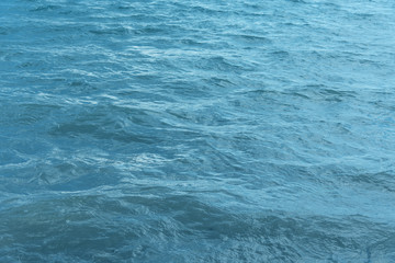 Blue water with waves and sun reflections background