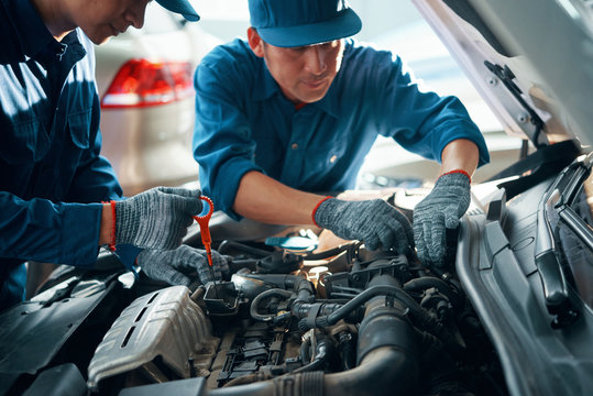 Mechanic measuring level of motor oil when his coworker checking pipes