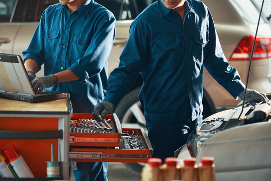 Cropped image of mechanic in uniform taking wrench out of draw when repairing car in garage