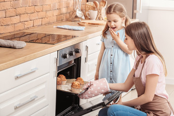Little girl and her mother baking muffins in kitchen