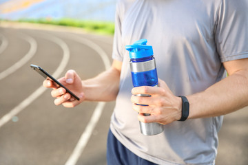 Sporty young man with mobile phone and bottle of water at the stadium