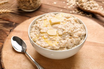 Bowl with tasty oatmeal on wooden board