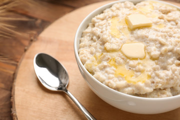 Bowl with tasty oatmeal on wooden board, closeup