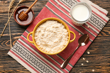 Pot with tasty oatmeal, milk and honey on wooden table