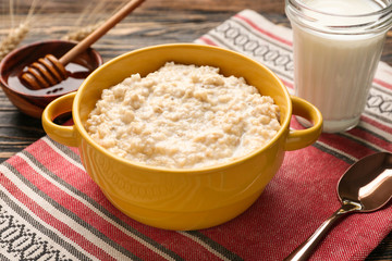 Pot with tasty oatmeal, milk and honey on table
