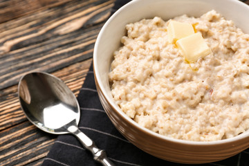 Bowl with tasty oatmeal on wooden table, closeup