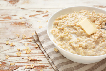 Bowl with tasty oatmeal on white wooden table