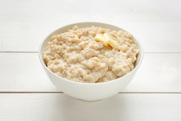 Bowl with tasty oatmeal on white wooden table