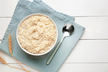 Bowl with tasty oatmeal on white wooden table