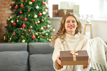 Happy young woman with Christmas gift at home