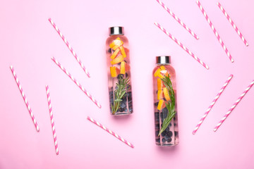 Bottles of tasty infused water and straws on color background