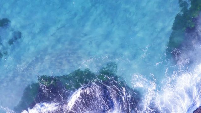 White fringed waves roll onto ocean rocks clear blue water bird flying across screen left of frame Tamarama beach Sydney Australia POV drone