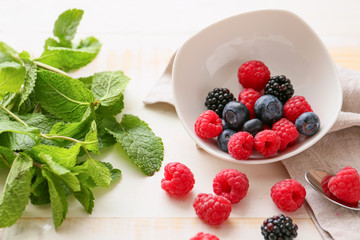Bowl with tasty ripe berries and mint on table