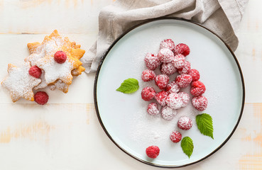 Plate with tasty ripe raspberries and cookies on white table