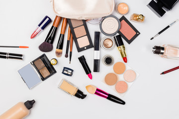 A pink makeup bag with cosmetic beauty products spilling out on to a light  background, with empty space at side