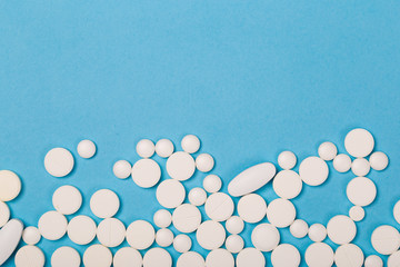 White Pills are scattered over a blue background. Close up. Medical background.