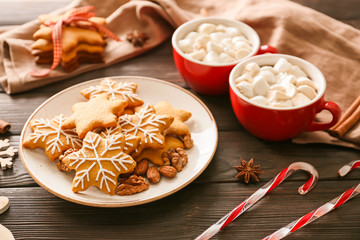 Plate with tasty Christmas cookies and cups of hot chocolate on wooden background