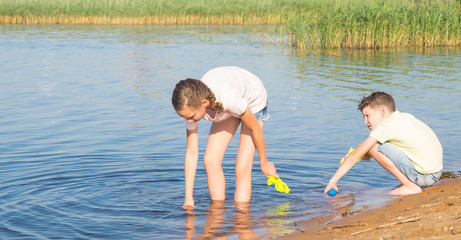 a girl and a boy collect water from a lake in water guns to play in them, against the backdrop of the landscape, close-up