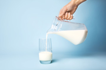 Woman pouring milk into glass on color background