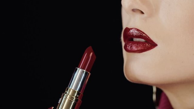 Closeup of female lips with red lipstick. Girl herself paints her lips with lipstick. In the studio on a black background. Bright makeup, clean skin. Passion. Lipstick with golden tube, case.