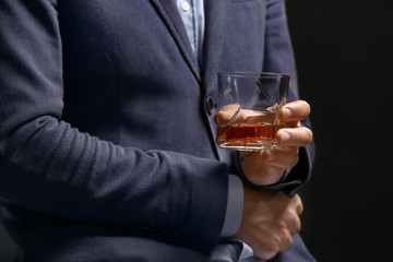 Businessman with glass of whiskey on dark background, closeup