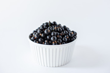 Ripe black currant or blueberries in a small white Cup on a white background. Black currant harvest. Healthy food. vegetarian food.