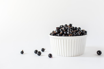 Ripe black currant or blueberries in a small white Cup on a white background. Black currant harvest. Healthy food. vegetarian food
