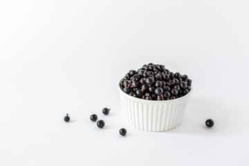 Fototapeta na wymiar Ripe black currant or blueberries in a small white Cup on a white background. Black currant harvest. Healthy food. vegetarian food