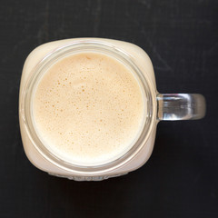 Peanut butter banana smoothie in a glass jar on a black background, overhead view. Top view, flat lay, from above. Close-up.