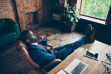 Dark skin minded guy dreamy looking through window holding legs on table wear elegant costume...