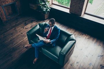 High angle photo of dark skin guy sitting office sofa drinking alcohol beverage reading fresh press wear elegant costume