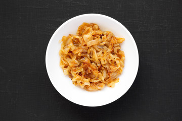 Homemade caramelized onions on a white plate on a black background, overhead view. From above, top view, flat lay.