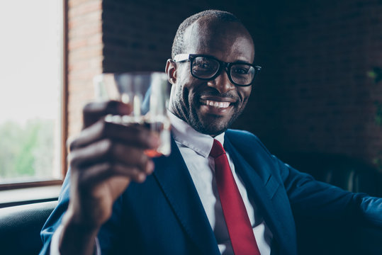 Photo of dark skin macho guy sitting office sofa drinking alcohol beverage wear specs and corporate costume