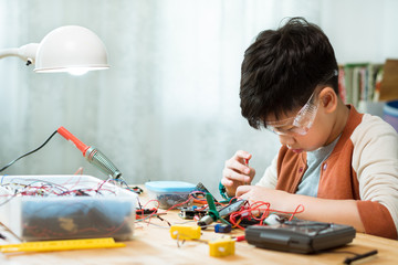 Smart preteen / teenage Asian boy screwdrivering, assembling and fixing computer chip, electronics...