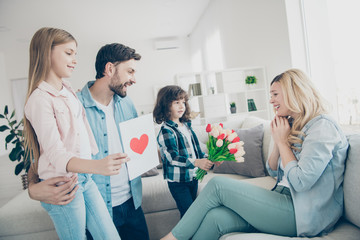 Young family dad and two children giving mom handmade card with fresh flowers emotional reaction