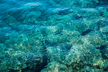 Turquoise sea surface with transparent shallow water - pebbles, stones, rocks on the seabed