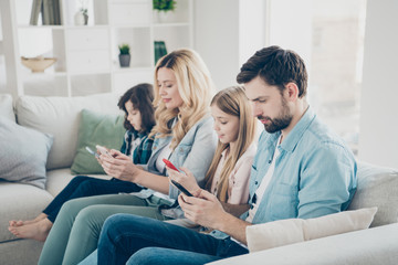 Fototapeta premium Young family two adopted children cozy sitting sofa look telephones don't care each other addiction concept