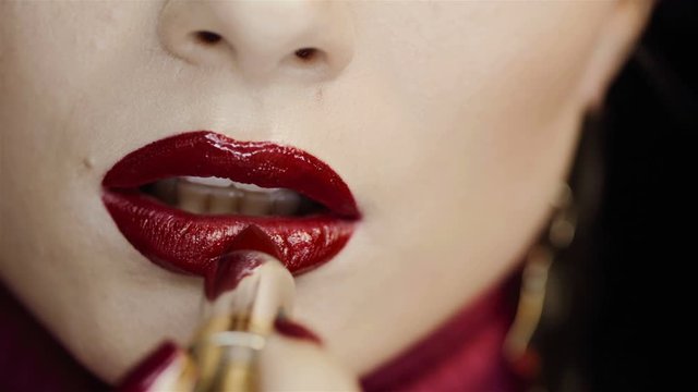 Closeup of female lips with red lipstick. Girl herself paints her lips with lipstick. In the studio on a black background. Bright makeup, clean skin. Passion. Lipstick with golden tube, case.