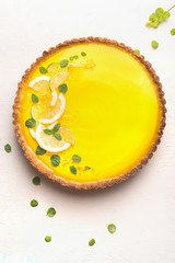 Lemon tart topped with citrus slices and zest on white table background, top view. Copy space....