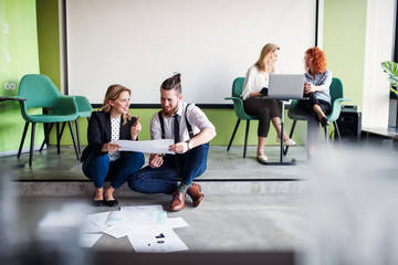 A group of young business people sitting on the floor in an office, talking.