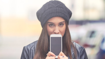 Young woman with hat holding cellphone in cold season on the street.