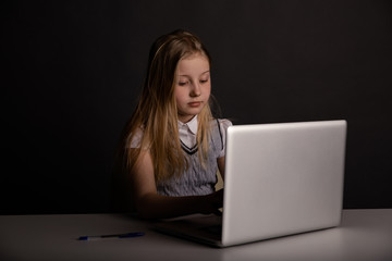 Bored little girl sitting on at the table and using computer isolated